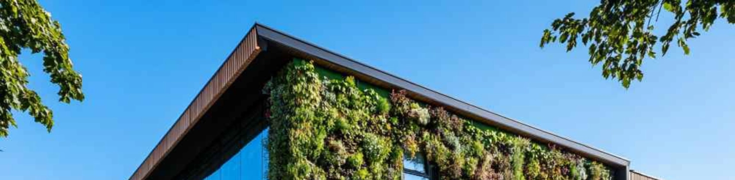 Bâtiment moderne avec un mur végétal, des arbres, une façade en verre et une journée ensoleillée.